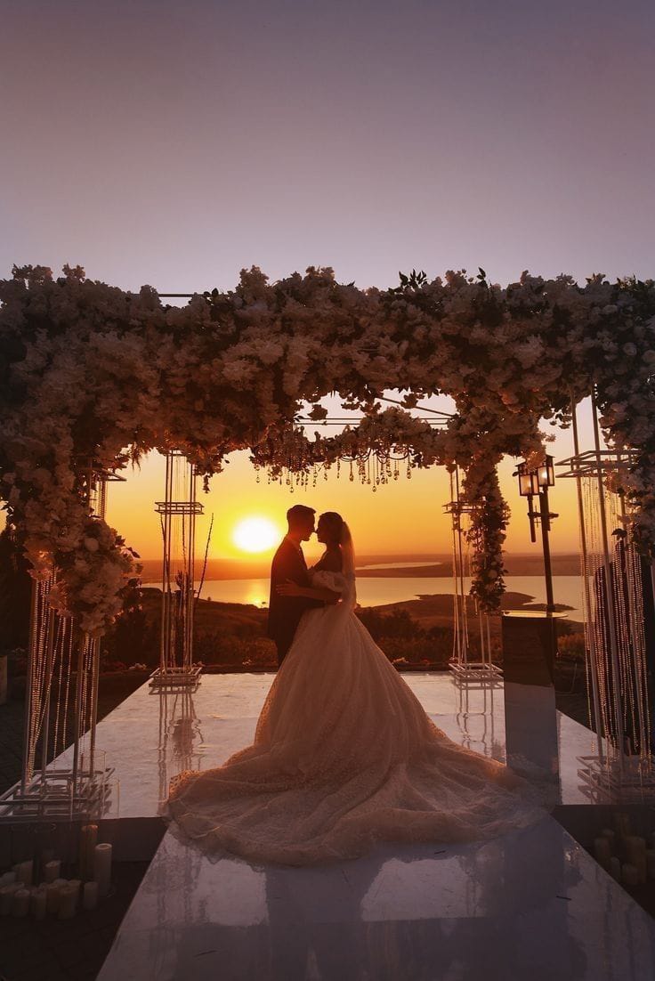 Bride and groom kissing under a floral arch at sunset