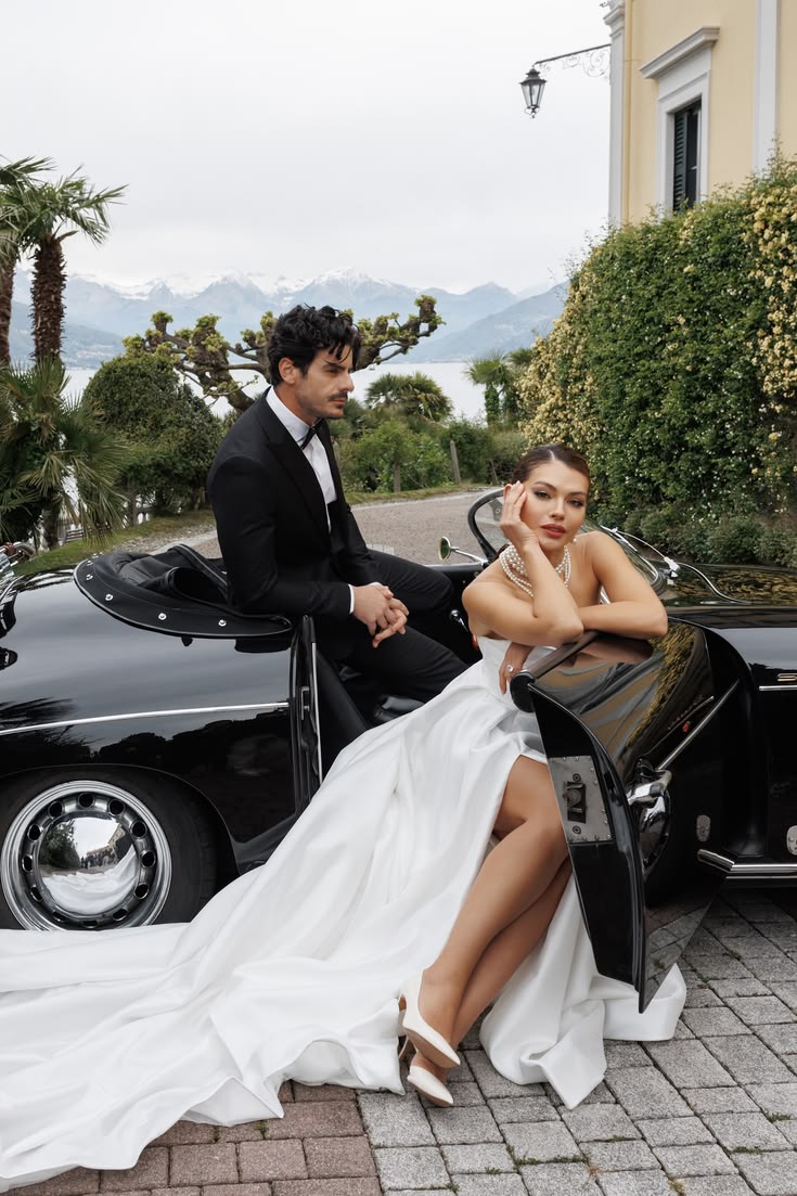 Bride and groom sitting on a vintage car outside a lakeside villa